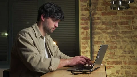 Focused man uses a laptop computer at home. Side view of a man in casual clothes 스톡 동영상 233284797