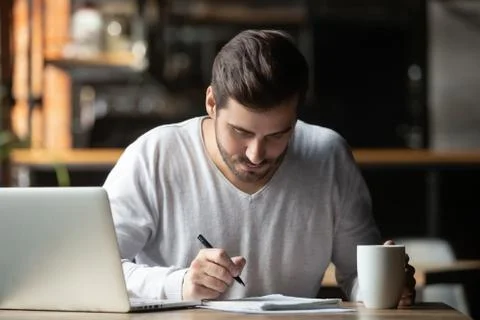 Focused man using laptop and writing notes in coffeehouse Stock Photos