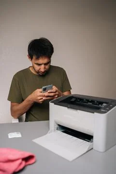Focused man using smartphone to read instructions while repairing laser printer 写真素材