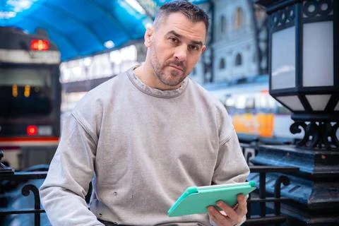 Focused Man Using Tablet While Waiting at Train Station looking at camera Foto stock