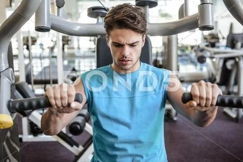 Focused man using weights machine for arms Stock Photos
