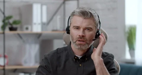 Focused Man wears Headset looking at the Camera and talking to Webcam Stock Footage 152407102