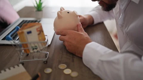 Focused man in white shirt shaking piggy bank at office desk to check its c.. Stock Footage 340143951