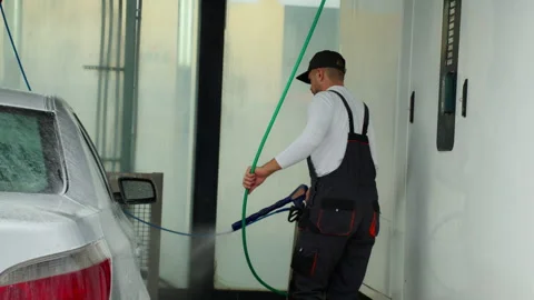 Focused man in work overalls cleaning silver sedan at self-service car wash.. Video stock 320889713