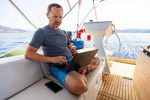 Focused man working on laptop aboard a sailing yacht. Productive remote office Stock Photos