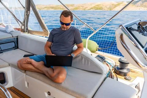Focused man working on laptop aboard a sailing yacht. Productive remote office Stock Photos