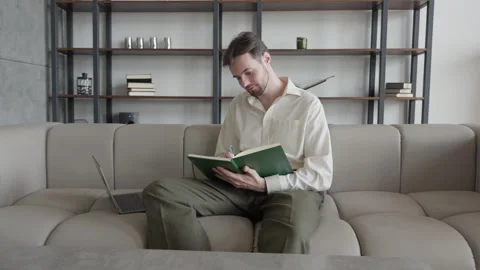 Focused Man Writing Notes In Notebook Sitting On Cozy Sofa, Studying Or Planning Stock Footage 303758758