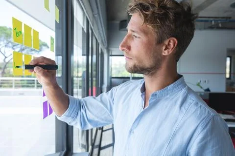 Focused man writing on sticky notes on office window, planning project tasks Stock Photos