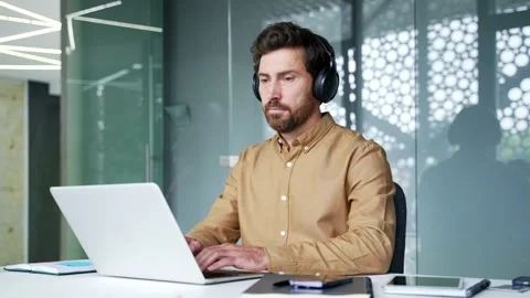 Focused mature software developer wearing headphones coding on a laptop at his  Video stock 342017937