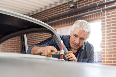 Focused mechanic using hammer on automobile hood in auto repair shop Stock Photos