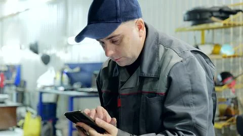 Focused mechanic using smartphone in garage, managing orders, checking Stock Photos