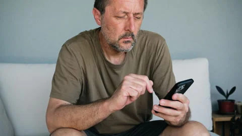 Focused middle-aged man using smartphone on couch at home checking messages.. Stock Footage 346808641
