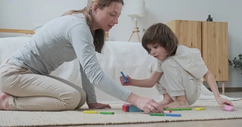 Focused mom teaching son kid constructing brick blocks wooden architecture at Vidéo 163251179