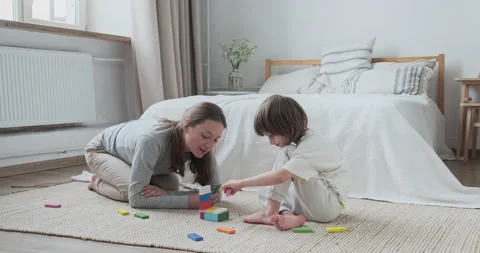 Focused mom teaching son kid constructing brick blocks wooden architecture at Stock Footage 164970871