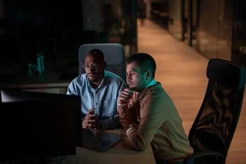 Focused multicultural team collaborating late at night, analyzing data and... Stock Photos