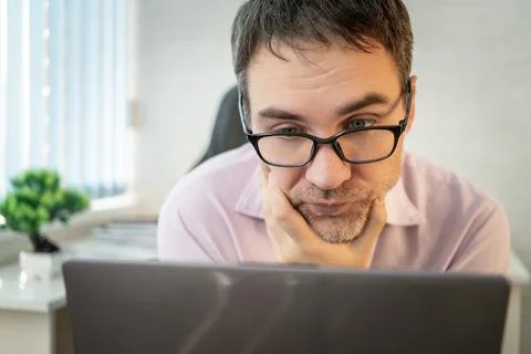 Focused office worker leaning on his hand, staring intently into a laptop scr Stock Photos