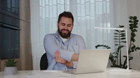 Focused online worker suffering from elbow ache while sitting by desk with pc Stock Footage 265213727