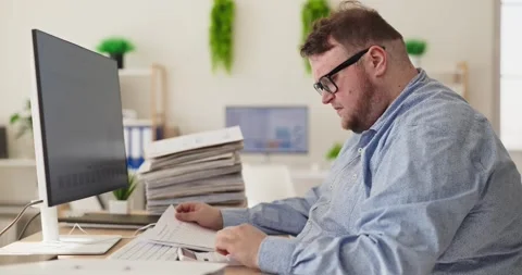 Focused overweight accountant reading paperwork at computer for budget analysis Stock Footage 335096685