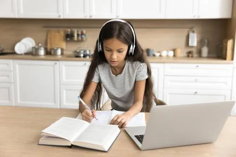 Focused pre teen schoolkid girl in headphones studying from home Stock Photos