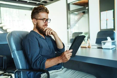 A Focused Professional Who is Analyzing Data on a Tablet in a Contemporary Stock Photos