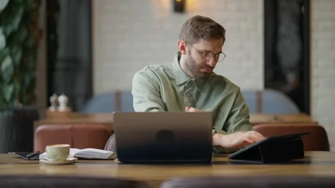 Focused Professional Working Remotely in a Modern Cafe Setting, Engaged with Stock Footage 344799819