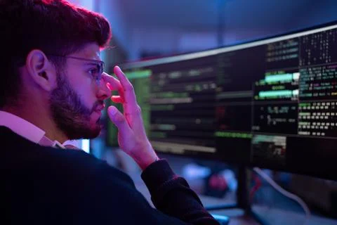 Focused programmer analyzes complex code on dual monitors in modern workspa.. Stock Photos