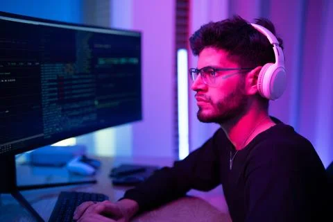Focused programmer coding at night with neon lighting and headphones in a m.. Stock-Fotos