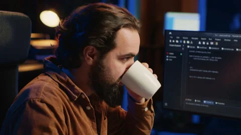 Focused programmer drinking coffee in apartment while solving database errors Stock Footage 265509919