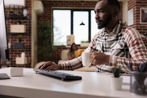 Focused programmer holding cup of coffee or tea looking worried at computer Foto stock