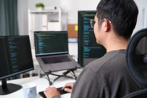 Focused Programmer Working on Code with Multiple Monitors in an Office Setup 库存照片
