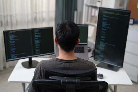 Focused Programmer Working with Multiple Monitors Displaying Code and Stock Photos