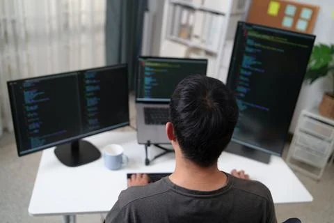 Focused Programmer Working on Multiple Monitors in an Office Environment to Stock Photos