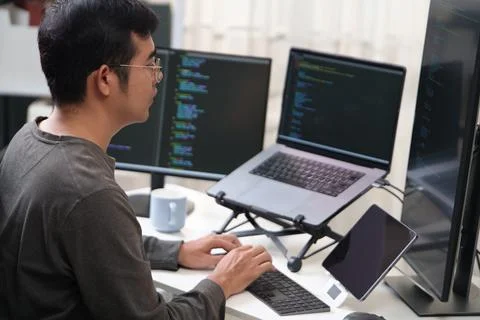 Focused Programmer Working on Multiple Screens with Code in an Office Setting Stock-Fotos