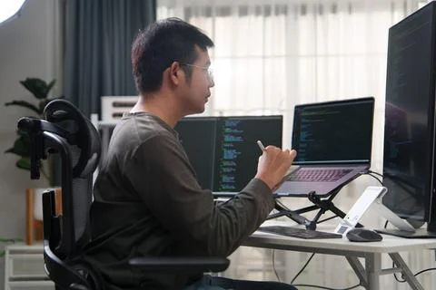 Focused Programmer Writing Code on Laptop and Desktop Monitors in Office Setu 库存照片