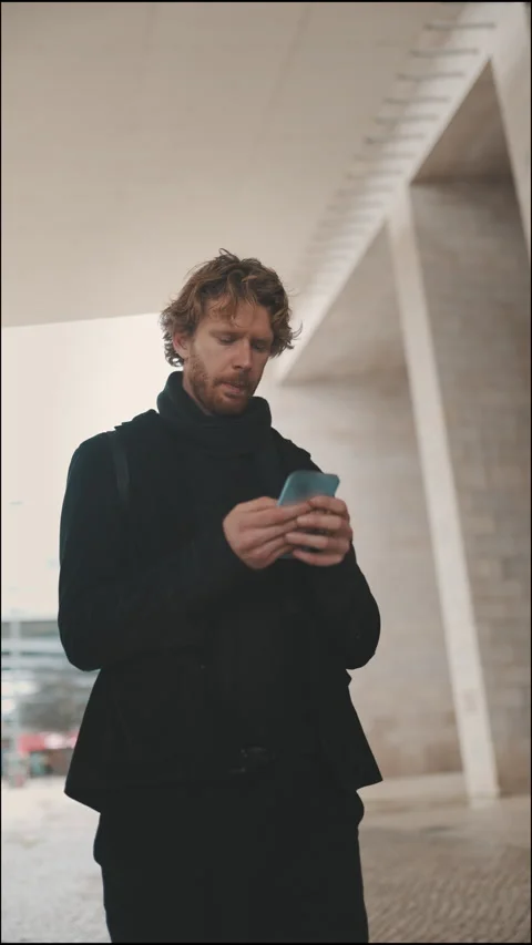 Focused redhead man using smartphone walking in urban setting Stock Footage 329018552