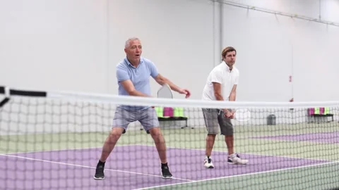 Focused resolved adult man playing friendly pickleball match in team with older Stock Footage 308750814