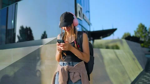 Focused schoolgirl browsing internet on mobile phone near glass facade. Zoomers Stock Footage 340479379