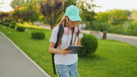 Focused schoolgirl walking in the park while reading on a digital tablet. Zoomer Video stock 340924654