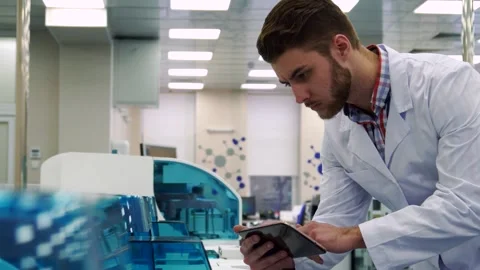 Focused scientist examines lab device using tablet Stock Footage 311820042