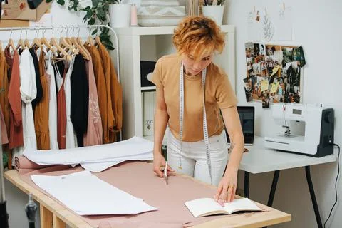 Focused seamstress checking patterns and notes on unrolled fabric on the tabl Stock Photos
