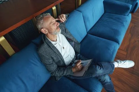 Focused senior analyst holding documents and looking at side sitting on sofa in Stock Photos