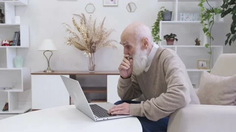 Focused senior man with long beard works online on modern laptop at desk Stock Footage 221650550