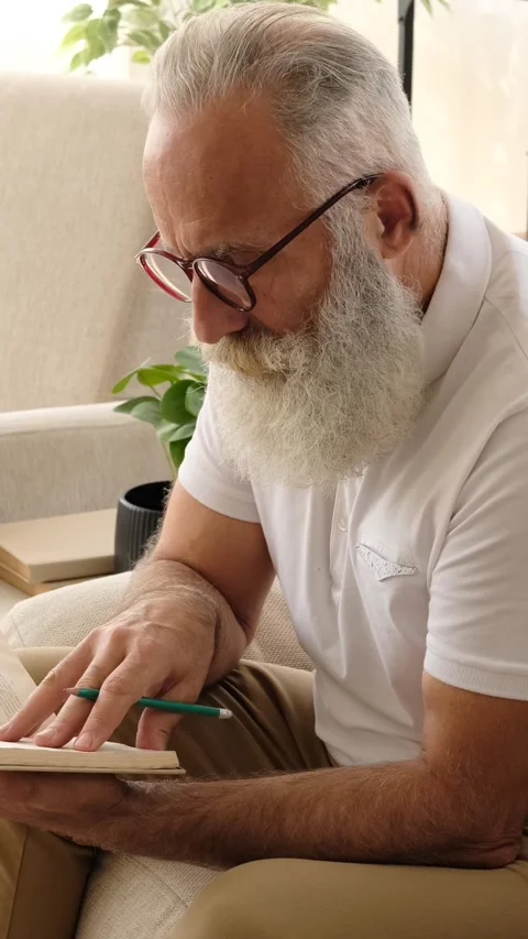 Focused senior man writing in a notebook at home Stock Footage 321140500