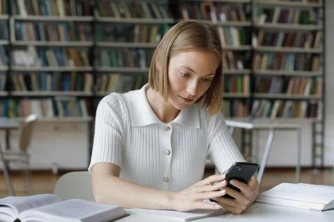 Focused serious female student using online app on mobile phone Stock Photos