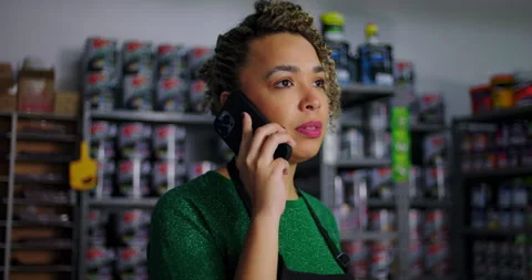 Focused shopkeeper on a phone call in a hardware store, shelves of paint and sup Stock Footage 318744493