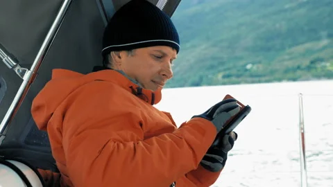 Focused smiling male tourist sitting in cabin of the yacht, writes a message Stock Footage 91096998