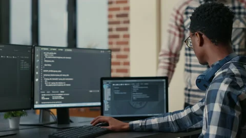 Focused software developer writing code on laptop looking at multiple screens Stock Footage 168250362