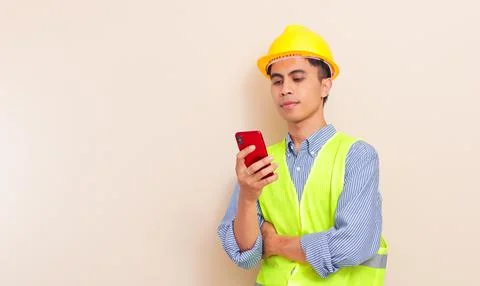 Focused Southeast Asian construction worker in hard hat and safety vest usi.. Stock Photos