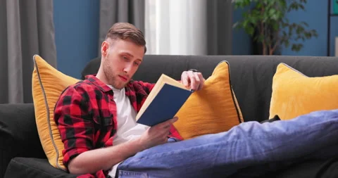 Focused student boy lay relax on couch at home reading interesting book, calm Stock Footage 154055574