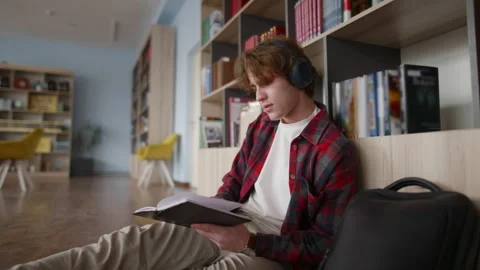 Focused student reading book and listening to music in library Stock Footage 331866908